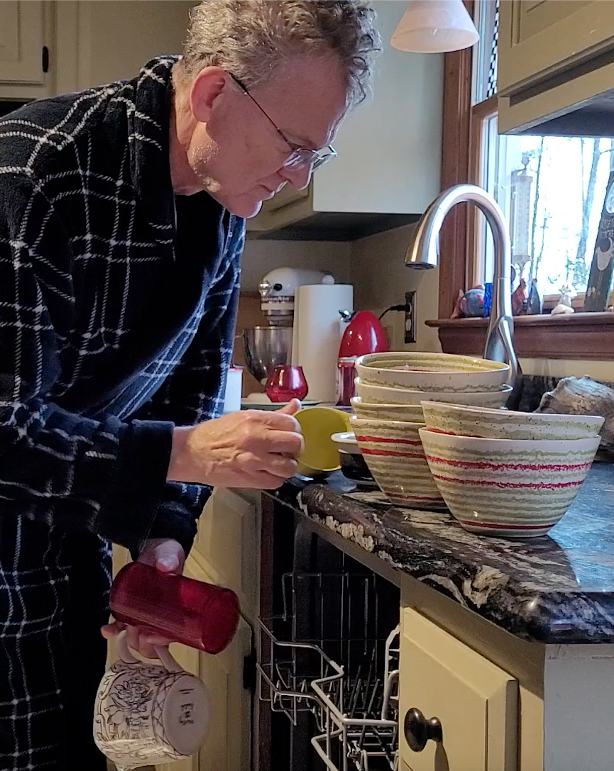 Scruffy man putting dishes away from dishwasher
