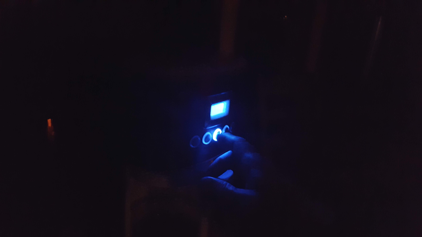 Finger pushes start button on a coffee maker in the dark.