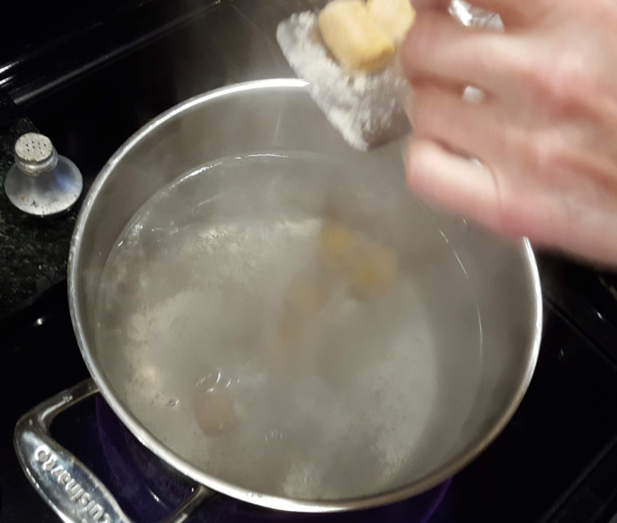 Gnocchi going into boiling water in a pan.