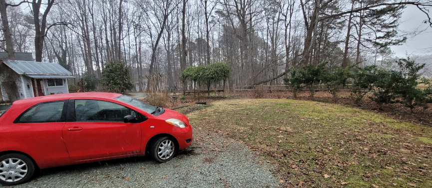 a backyard, with red car in a driveway.