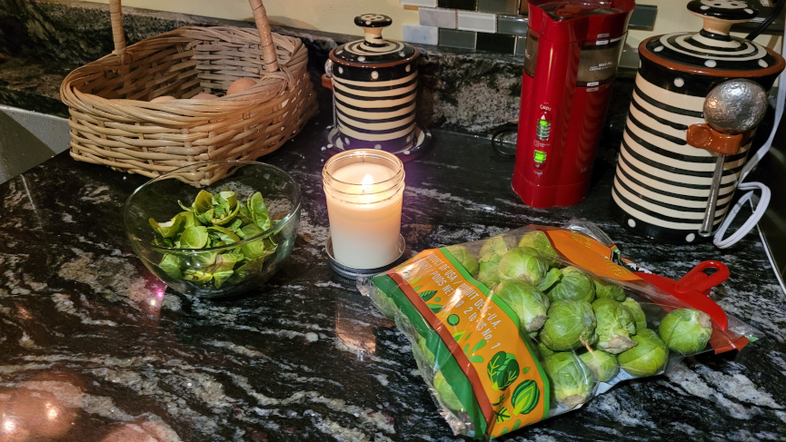 a candle lit on a butcher block with vegetables in bags.