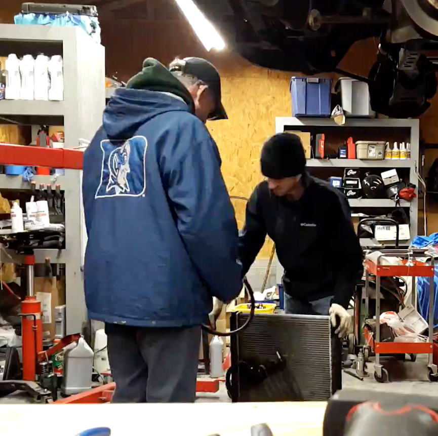 Two men looking at a car radiator in a garage.